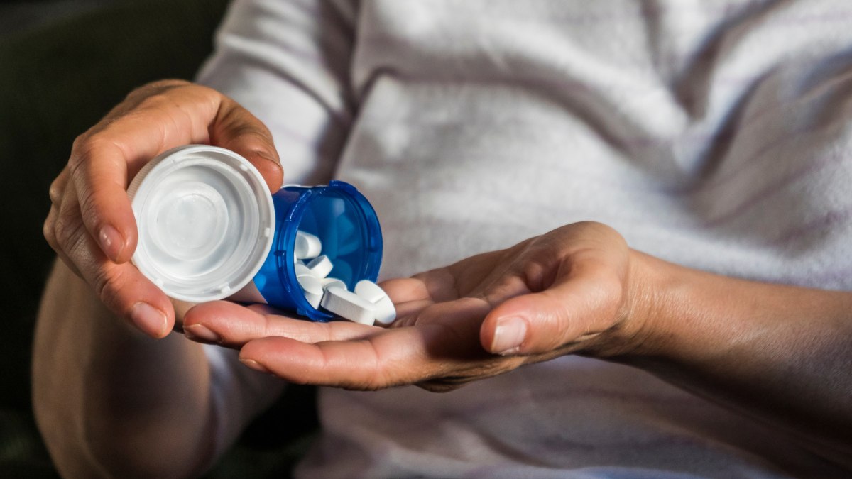 Woman pouring white pills into her hand.