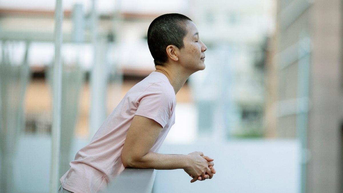 Woman taking a deep breath in, leaning off of a balcony.