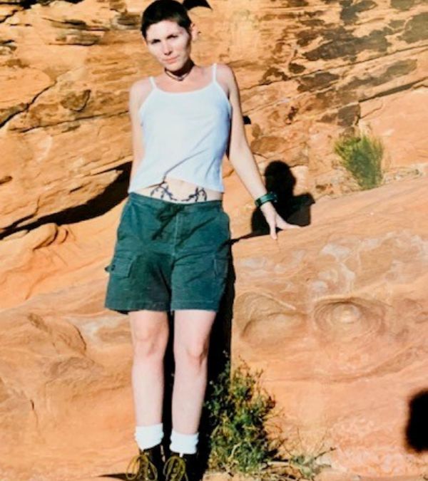 Lauren Izzo as a younger woman wearing shorts and hiking boots in a rocky terrain
