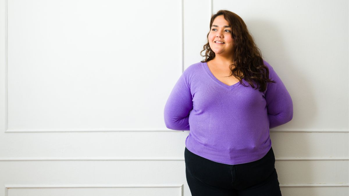 Woman standing against a wall, smiling.