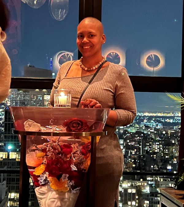 Angel Rinker stands smiling brightly behind a flower-filled glass table