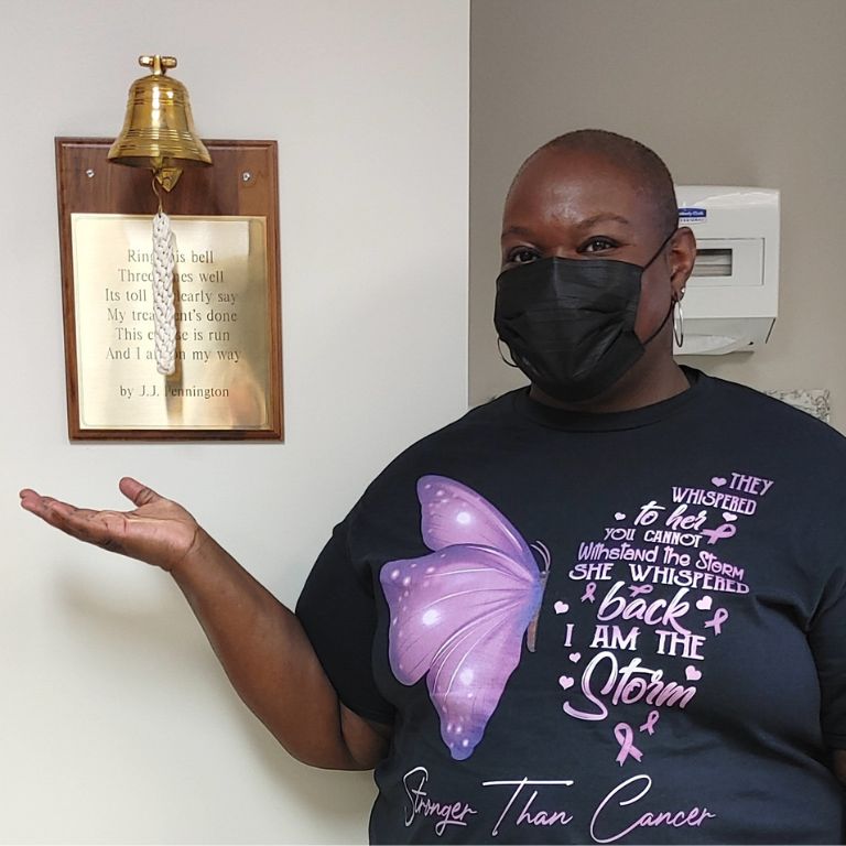 Ebony-Joy Igbinoba masked-up next to the cancer bell at her hospital.