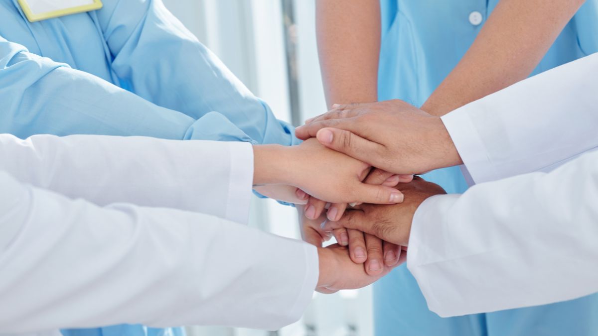 Four healthcare professionals with their hands on top of each other.