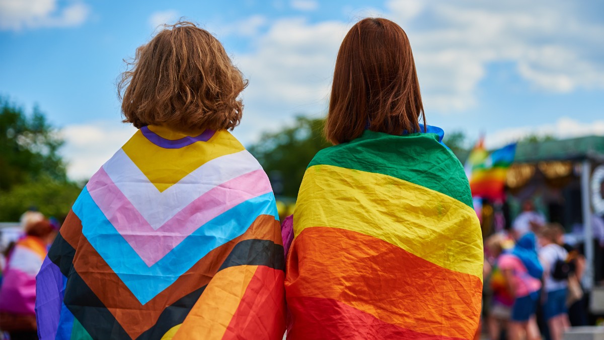 Two people with their backs turned, wrapped in pride flags.