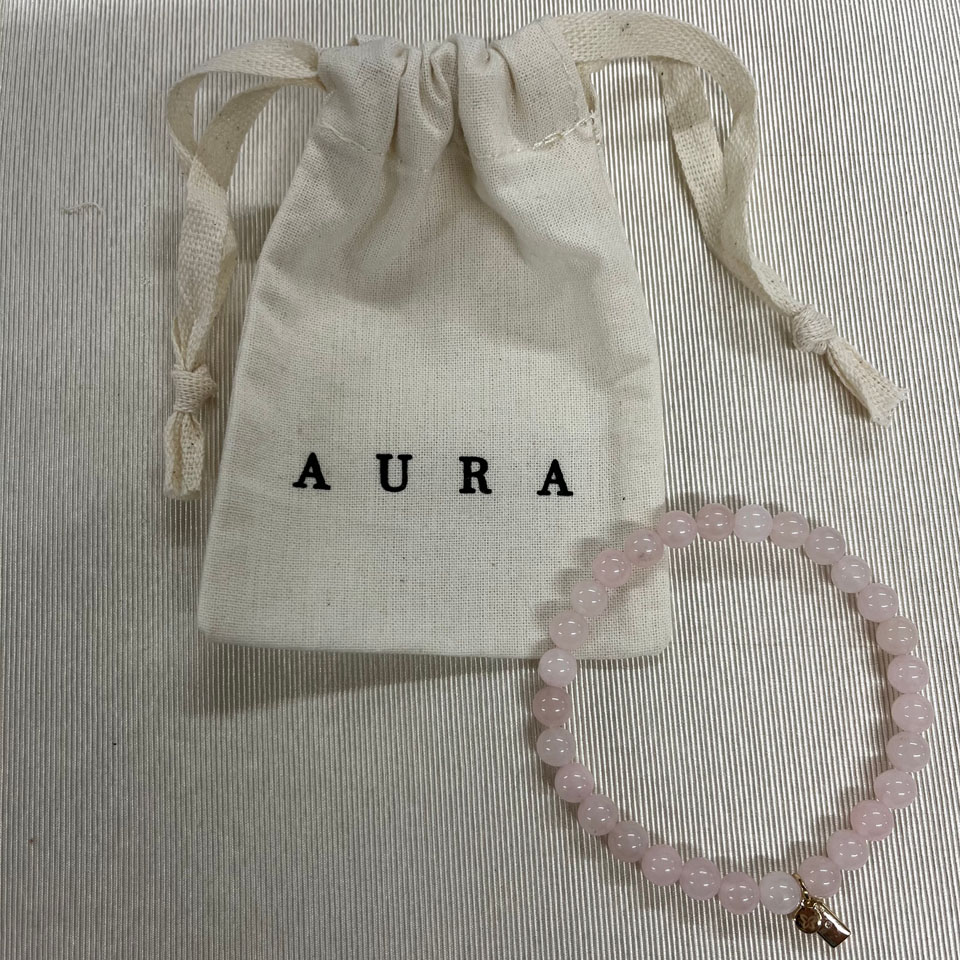 A pink bead bracelet with a small gold charm next to a small fabric bag