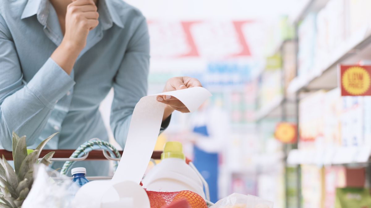 A woman leans over her shopping cart, examining her receipt as she leaves the grocery store