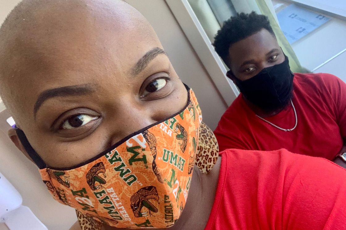 Jonise Louis wears a mask; her husband, also wearing a mask, looks lovingly behind her shoulder