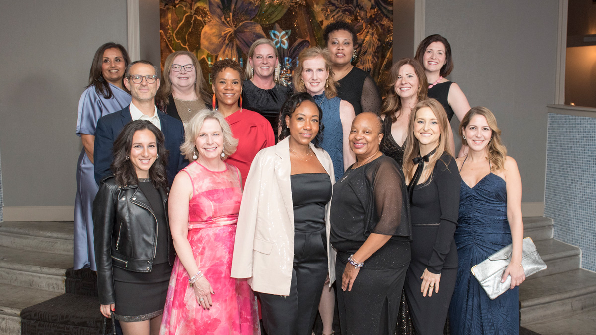 A diverse group of men and women dressed up and smiling on steps at the Butterfly ball.