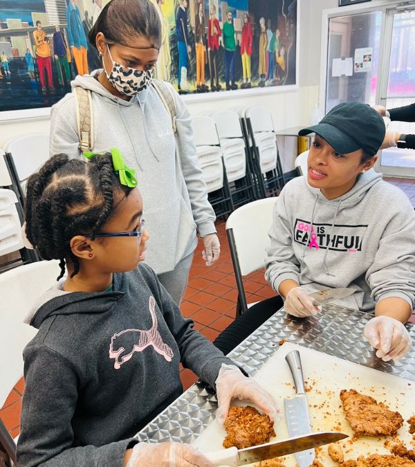 The Dedmon family volunteers at a food kitchen, cutting fried chicken into quarters.
