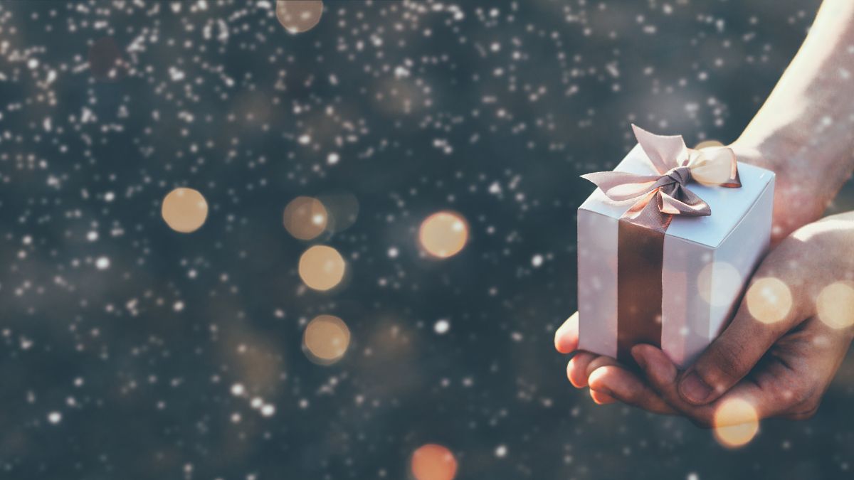 Gold sparkles against a blue background and hands reach out to offer a wrapped present.