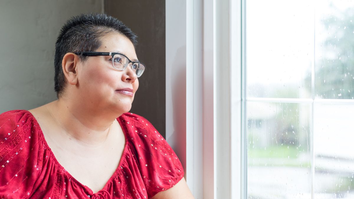 A woman with short hair and glasses staring out a window.