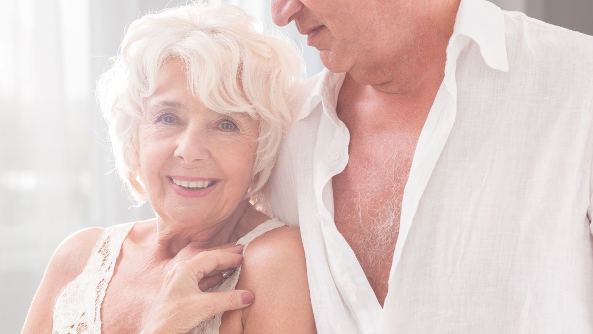 An older woman in a bra, smiling next to an older man with an unbuttoned shirt.