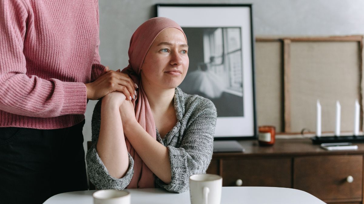 A woman sitting at a table, being comforted by a woman off camera.