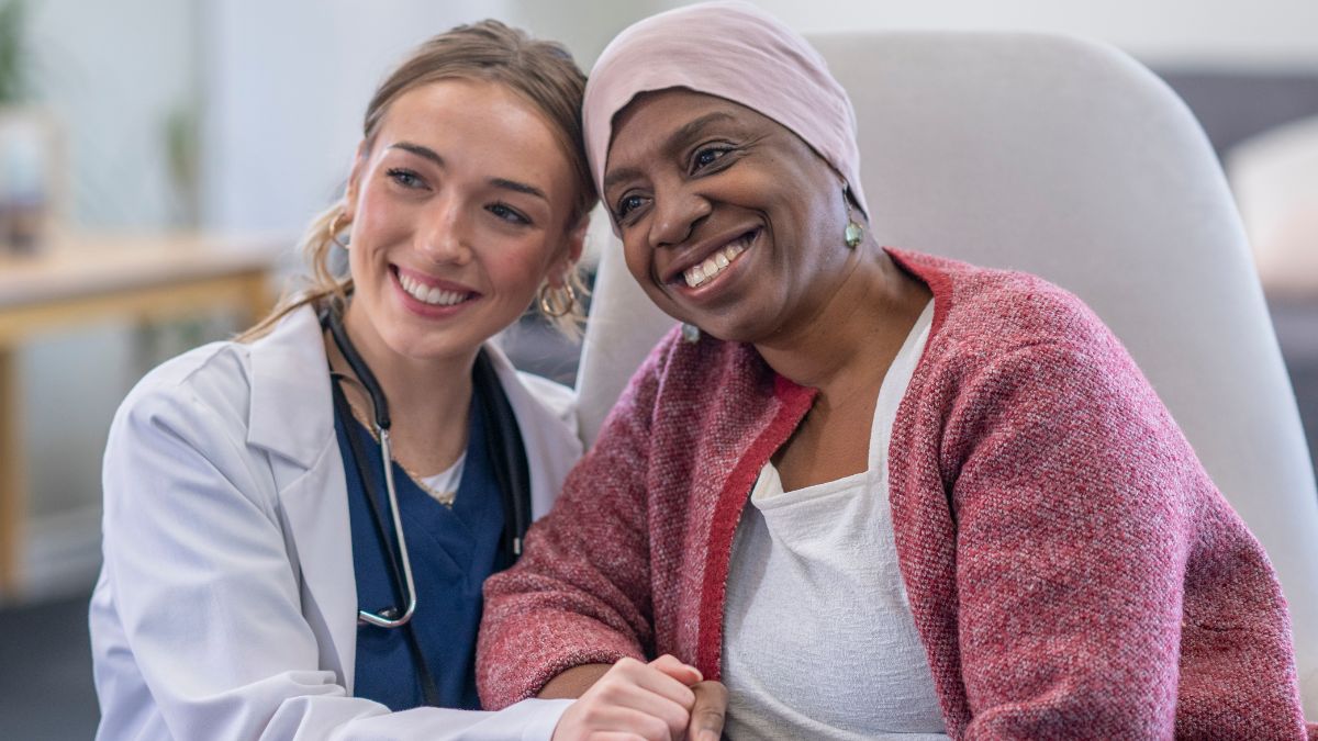 A white doctor and Black breast cancer patient smiling and holding hands.