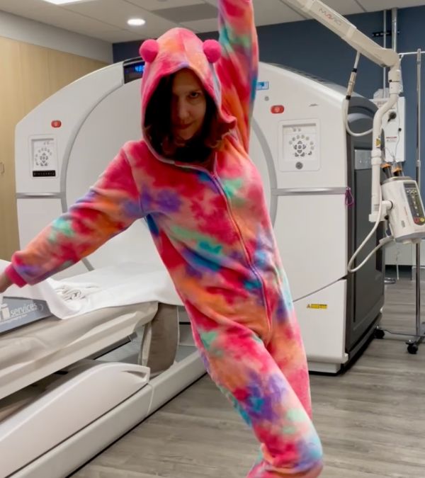 In a CTscan room, Bethany Adair dances as she wears a tie-dye bear outfit.