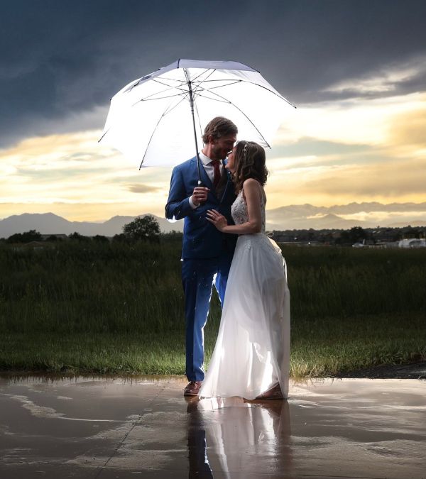Light illuminates a white umbrella which shelters Bethany Adair in her wedding dresses and her new husband.