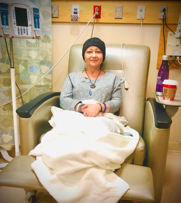 Jenna sits in a chemo chair, a blanket keeping her warm and cozy.