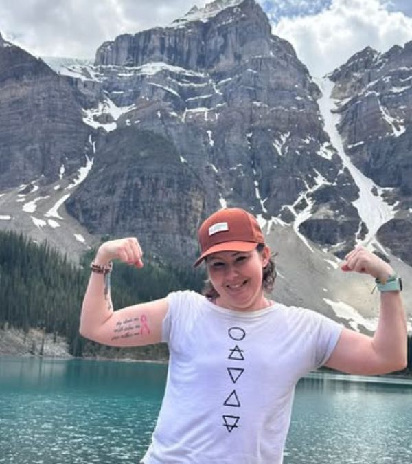 Julie Rock poses, her arms flexed, in front of a gorgeous mountain.