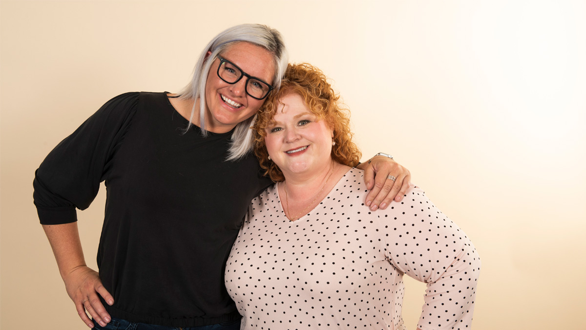 A young white woman smiling with her arm around an older white woman who is also smiling.