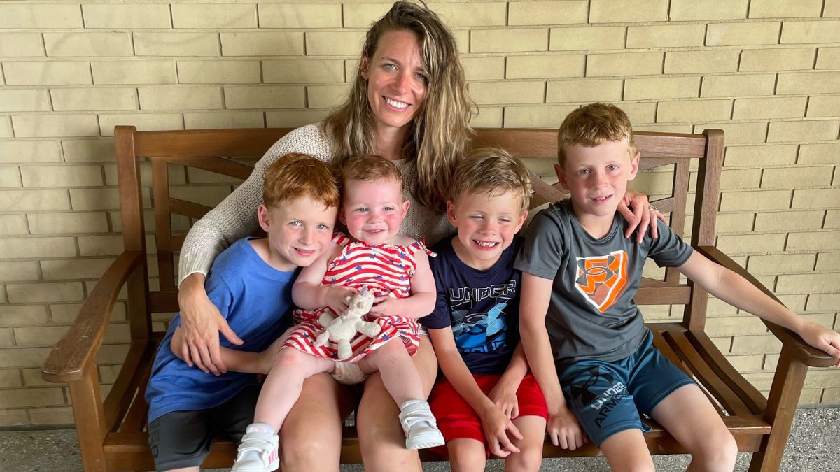 Karen Powell sits on a bench, her arms gathered around her four young and grinning children.