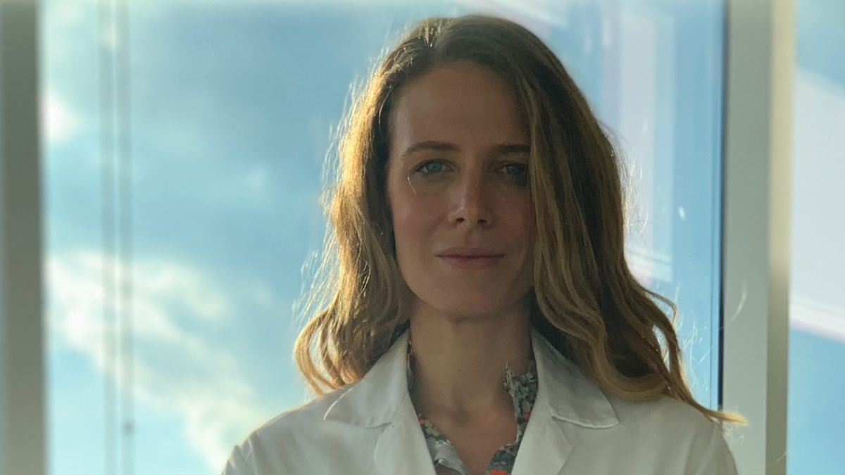 Karen Powell stands against a large window in her white nurse's jacket.