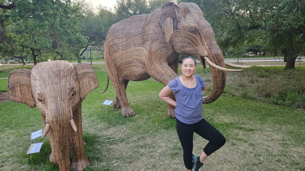 Christina Jue strikes a yoga pose in front of two realistic and beautiful elephant sculptures.