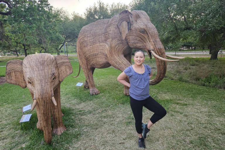 Christina Jue strikes a yoga pose in front of two realistic and beautiful elephant sculptures.