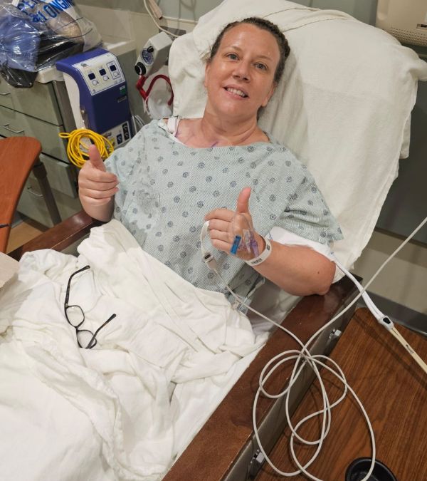 Kendra Ajuba gives two thumbs up from her hospital bed after breast cancer surgery.