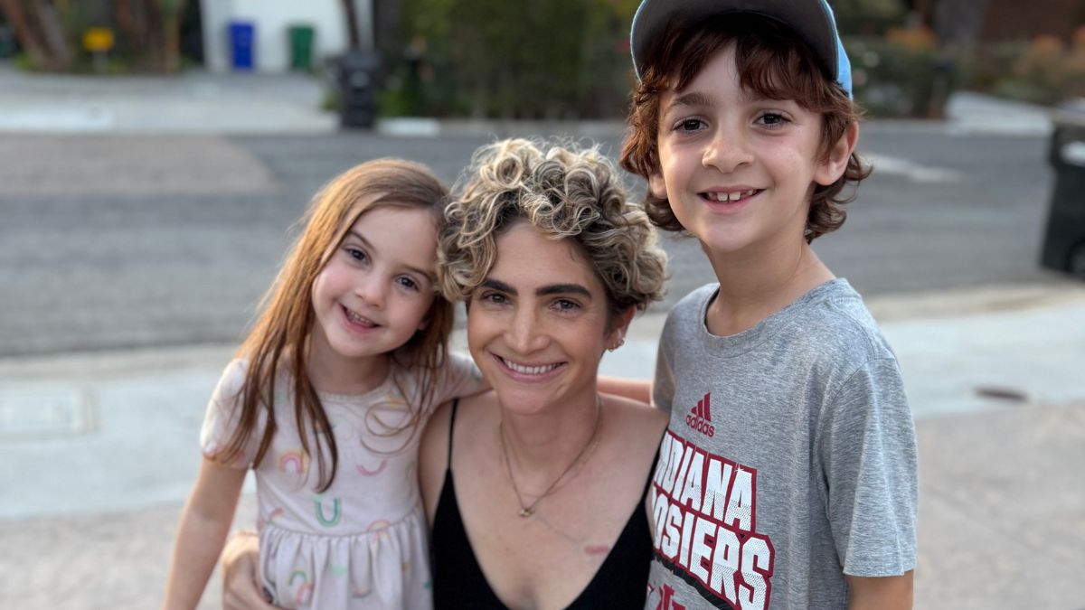 Lilly Ribner kneels on the sidewalk as she hugs her two small children close to her, their close bond evident.