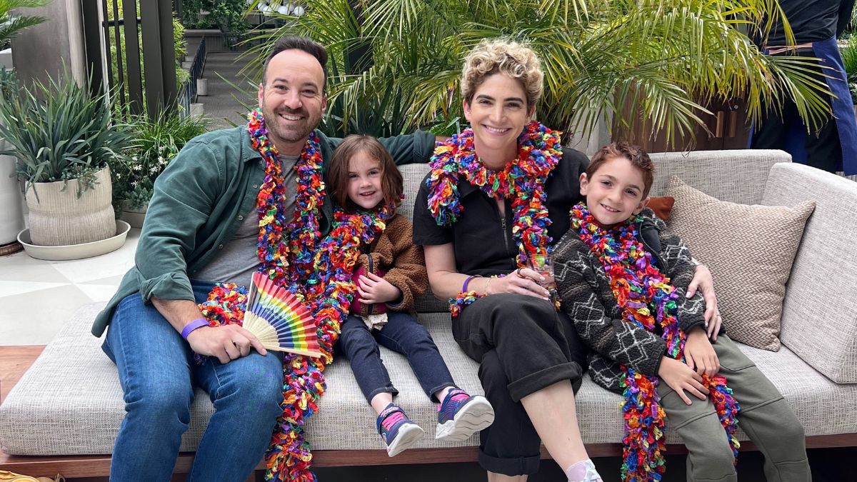 Lilly Ribner, her husband, and their two young children sit happily in an outdoor patio, wearing colorful scarves.