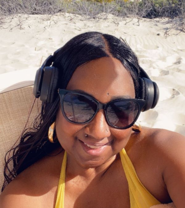 Stephani St. Cyr listens to music on her headphones as she sits on the beach in a yellow top.