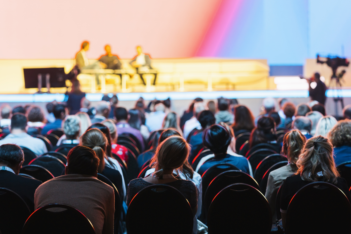 A crowd of people in seats, looking toward a stage.