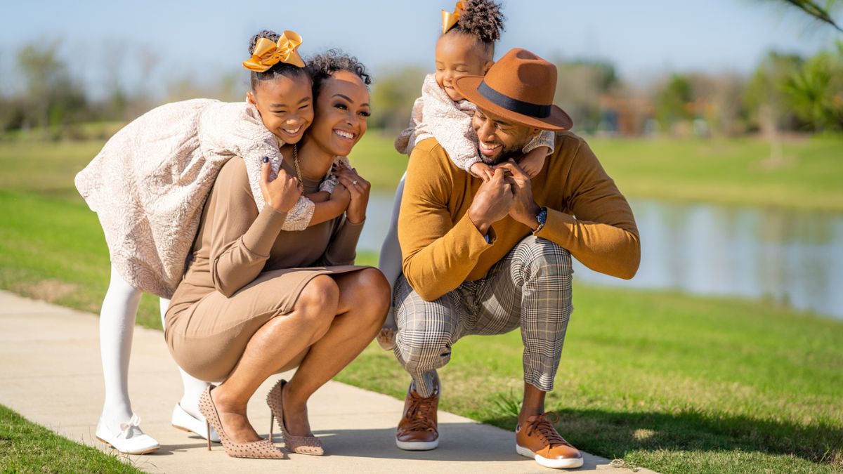 Ashley Dedmon and her husband stoop on the sidewalk to pick up their daughters on their backs.