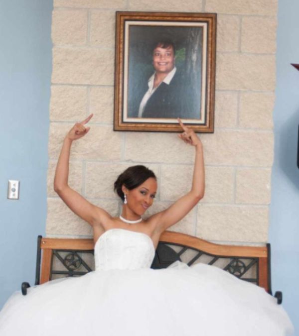 Ashley Dedmon, dressed in white gown, points up triumphantly at a portrait of her late mother.