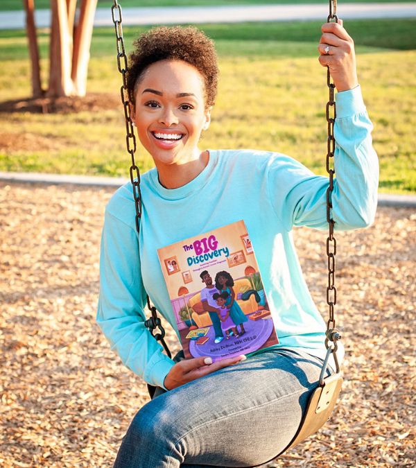 Ashley Dedmon sits on a swing holding her book, "The Big Discovery."