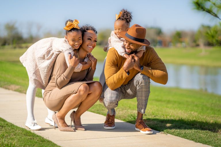Ashley Dedmon and her husband stoop on the sidewalk to pick up their daughters on their backs.