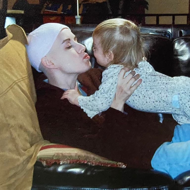 Klara Hartfiel kisses her baby daughter as she rests on the couch during her breast cancer treatment.