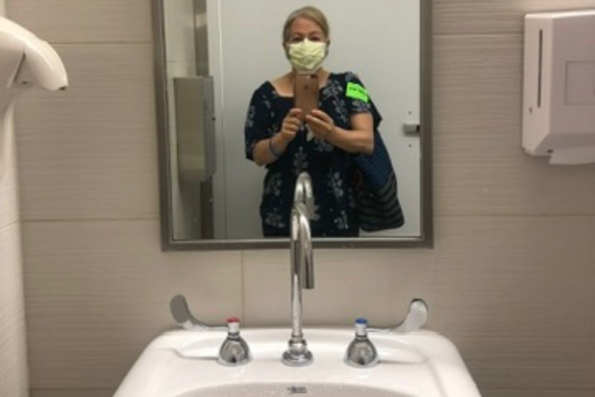Maria Lleonart documents her second round of chemotherapy in the clinic's bathroom, the sink prominent under the mirror displaying her reflection.
