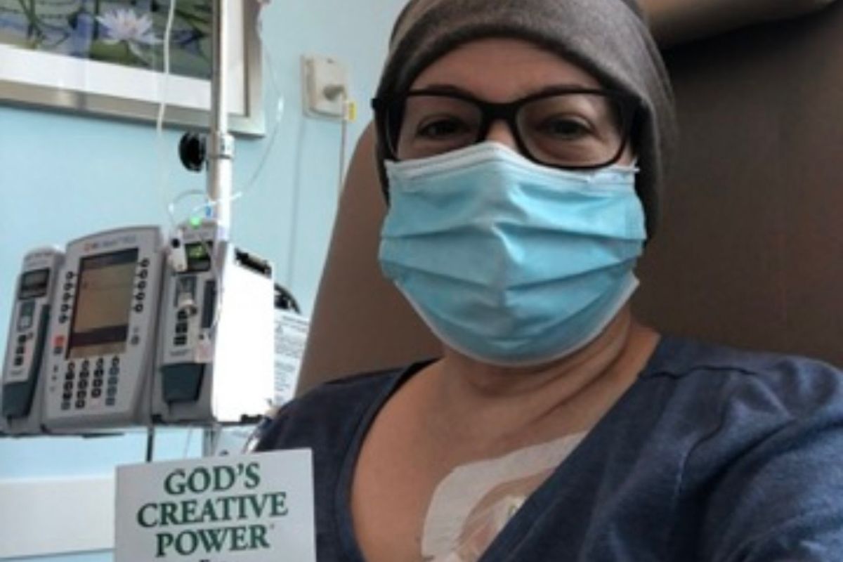 Maria Lleonart wears a beanie and a mask as she receives chemotherapy and reads a religious book.