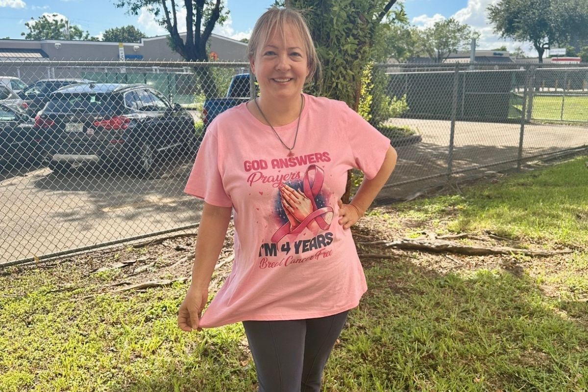 Maria Lleonart stands in her backyard wearing a pink breast cancer survivor t-shirt.