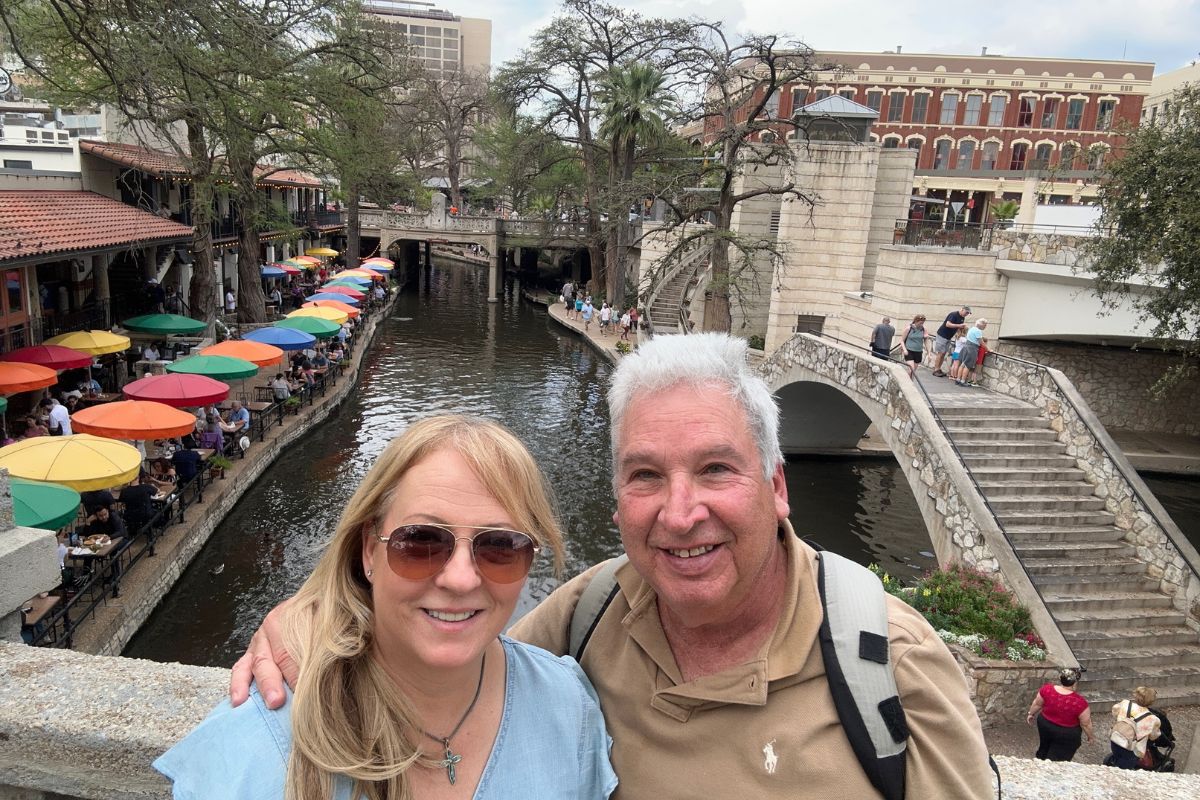 Celebrating her 60th birthday, Maria Lleonart and her husband share happy smiles on a festive street in Texas.