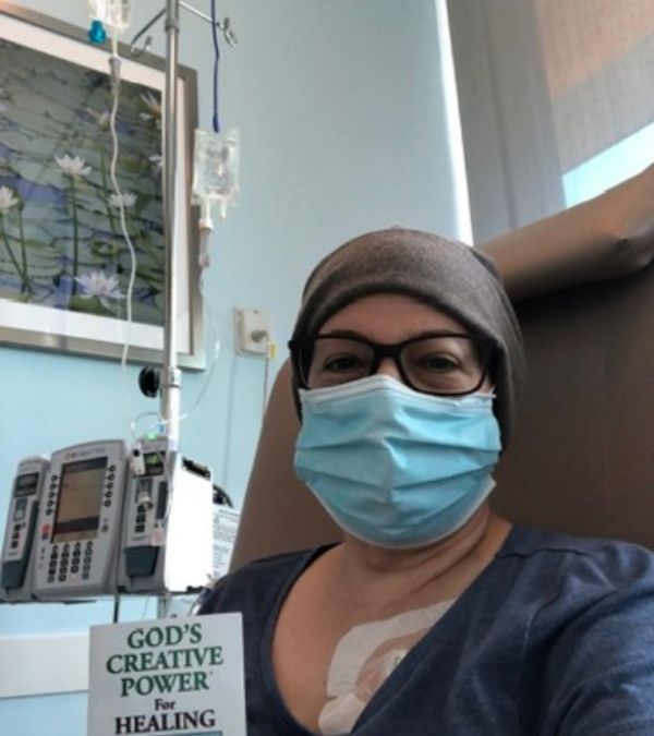 Maria Lleonart wears a beanie and a mask as she receives chemotherapy and reads a religious book.
