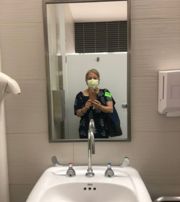 Maria Lleonart documents her second round of chemotherapy in the clinic's bathroom, the sink prominent under the mirror displaying her reflection.