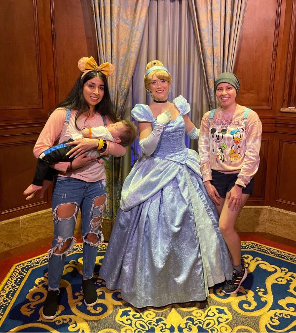 Marisa Espinosa stands alongside a real life Cinderella at Disney. Her relative stands on the other side of Cinderella holding a baby.