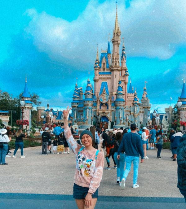 Marisa Espinosa waves happily as she stands in front of the Disney castle.