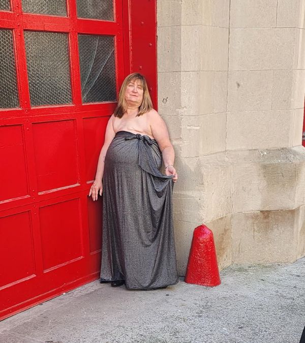 Amy Russell-Parliman, who had a double mastectomy and has metastatic breast cancer, stands against a bright red fire engine door, exposing her chest in a long gray gown.