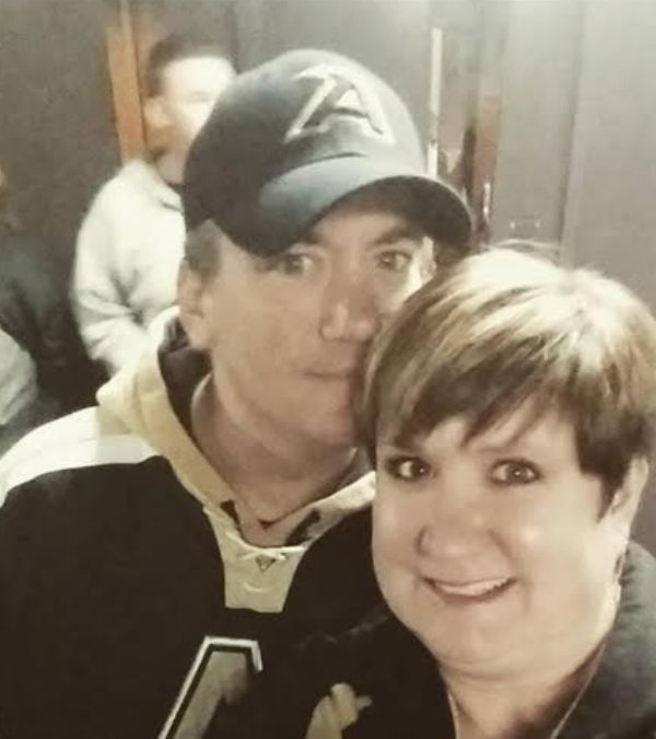 Amy Russell-Parliman stands close with her husband, their bond evident as he touches his chin to her head and she smiles.