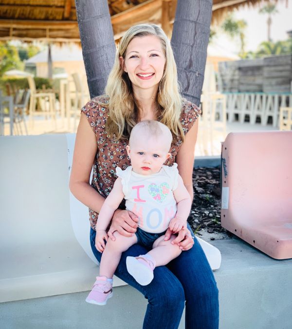Kara Taylor holds her baby daughter under a tropical hut.