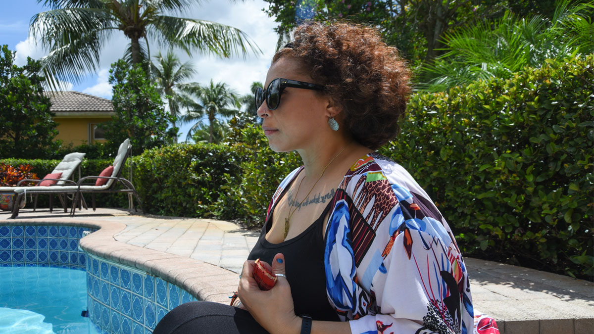 A Latina woman sitting poolside with a fan in her hand.