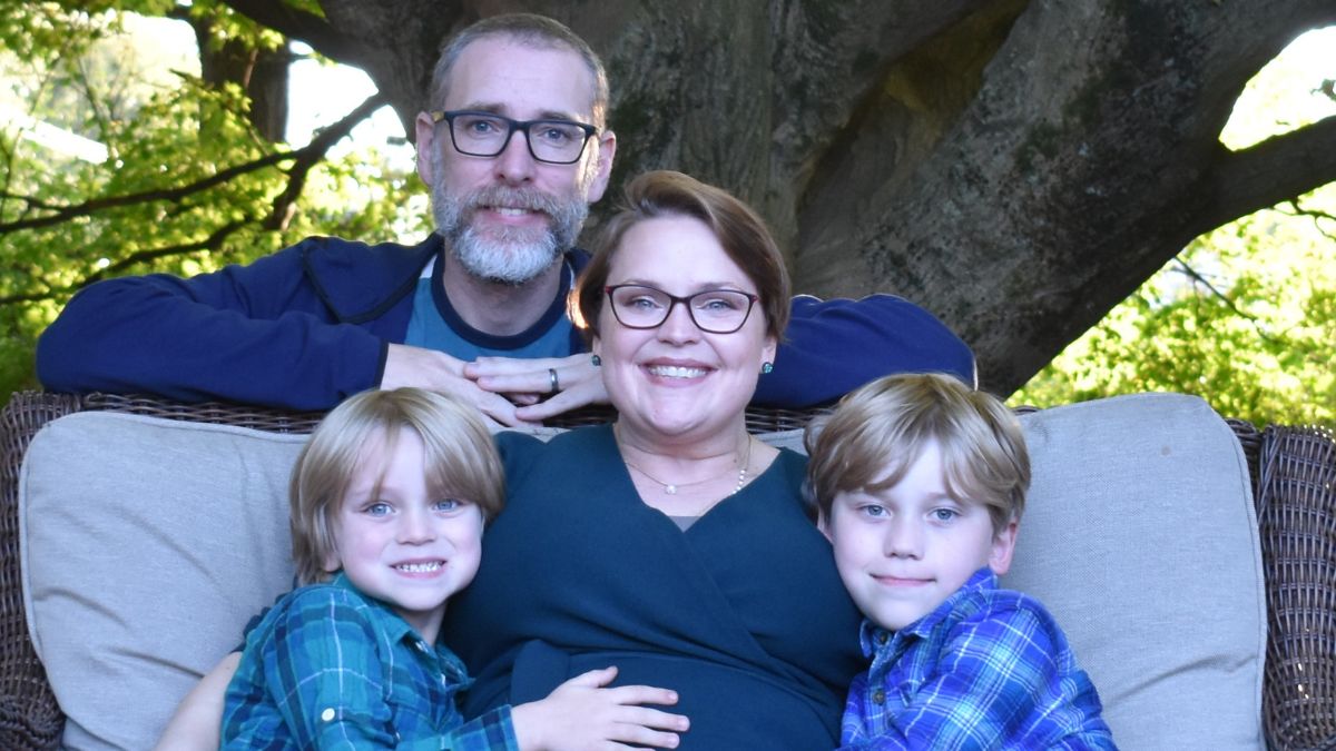 Her hair growing in after chemo treatment, Charlotte Safrit hugs her two children close, her husband behind her, a tree offering them shelter on a beautiful day.